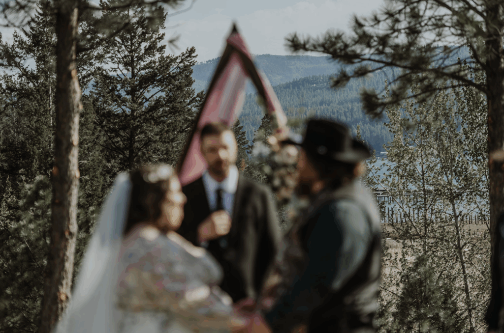 A photo showing an example of documentary-style wedding photographer. A bride, groom, and officiant are out of focus in the foreground and with a Montana mountain range in focus behind them.