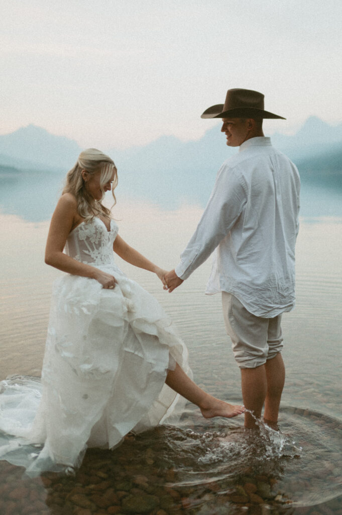 A wedding photo that feels authentic of a bride and groom wading in a lake.